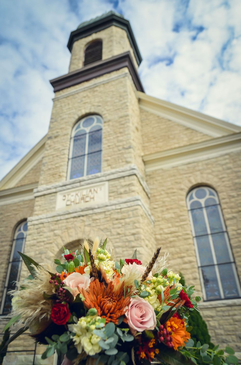 Beautiful fall flower arrangement with roses and lilies in front of a historic stone church with arched windows.