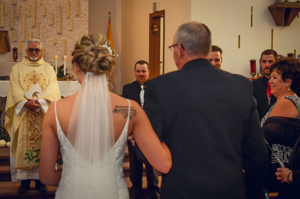 Bride and guests gather at the altar during a traditional Catholic wedding ceremony with a priest in white robes.