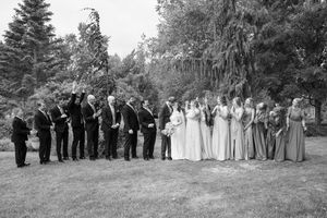 A black and white photograph of a wedding party lined up outdoors with trees in the background.