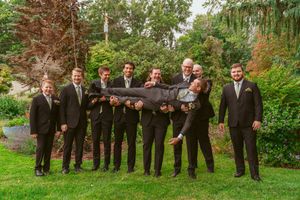 Wedding party groomsmen lined up outdoors wearing dark suits in autumn garden setting.