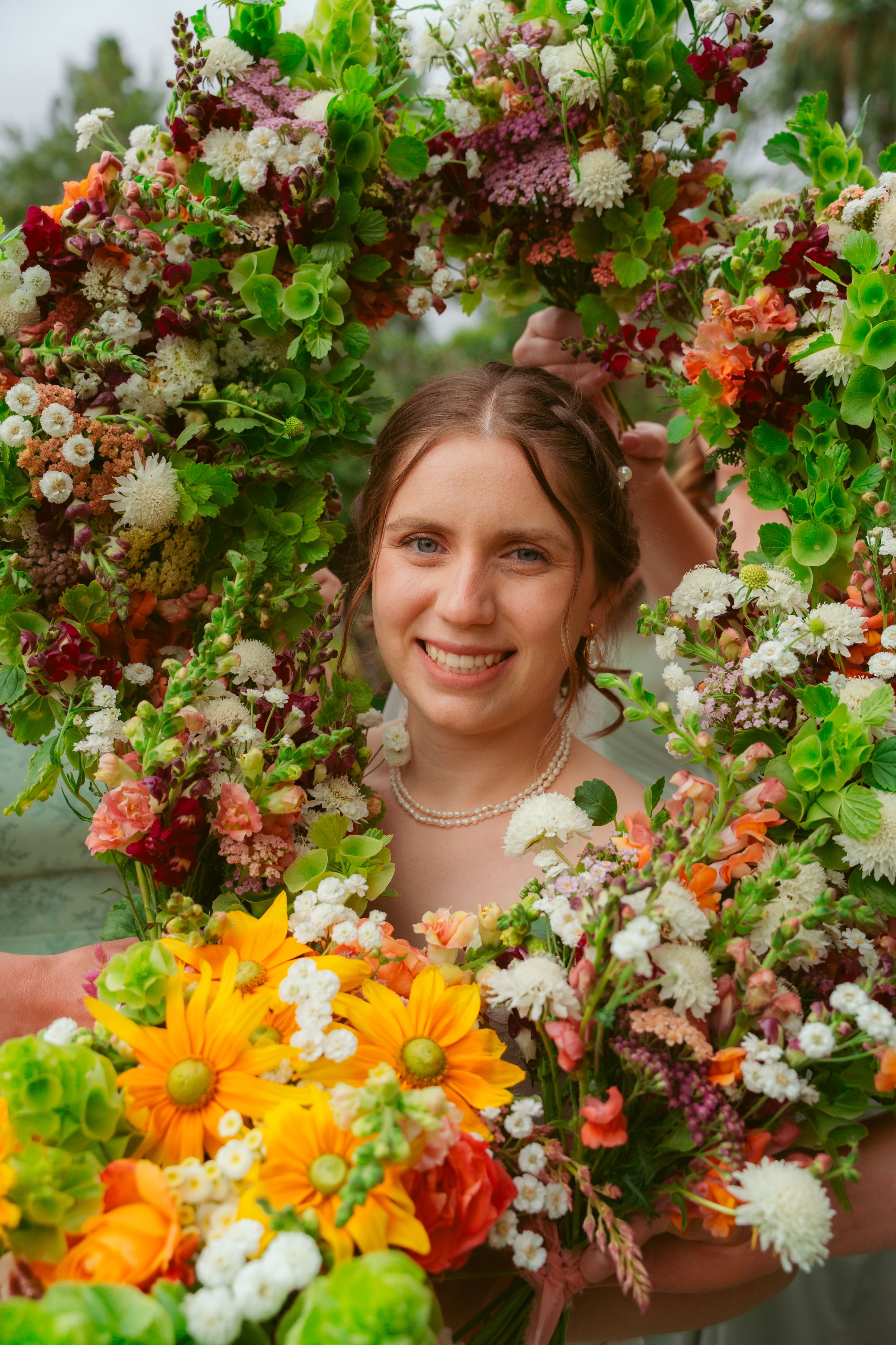 Beautiful floral arrangement with vibrant orange daisies and mixed flowers framed by a lush foliage arch in an outdoor setting.
