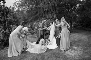 Black and white photo of wedding party members arranged artistically on grass for formal portraits.