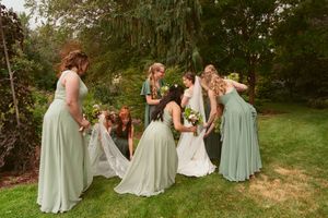 A group in sage green dresses gathers together on a grassy lawn during a wedding celebration.