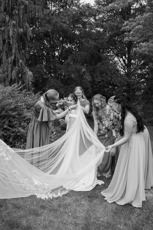 Bridesmaids in flowing dresses help arrange the bride's dramatic white train for a creative photo.