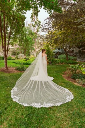Dramatic cathedral length lace wedding dress train spread out on green grass in garden setting.