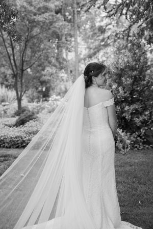 Black and white photographs show the flowing train of a bride's wedding dress against a garden backdrop.