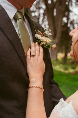Close-up of wedding rings and jewelry details with hands against a dark suit.