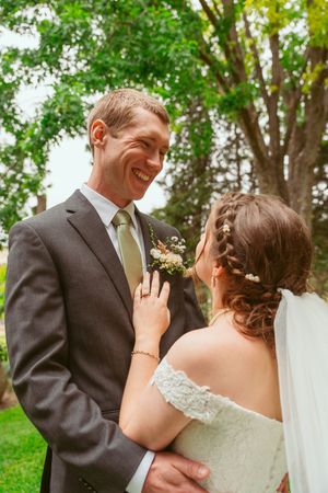 A romantic wedding couple shares an intimate moment beneath towering green trees on their special day.