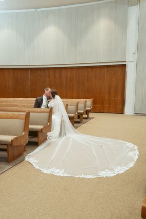 A stunning cathedral-length wedding veil with lace detailing spreads across a church floor in a series of photos.