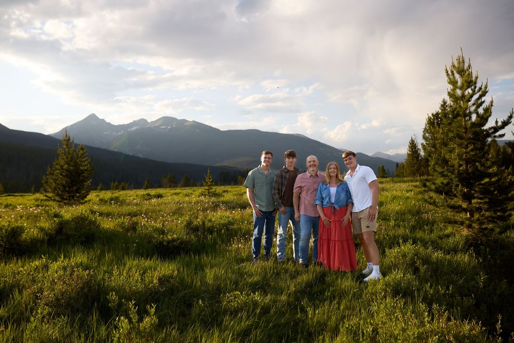 A group poses along a grassy hillside overlooking mountain landscapes during golden hour with long shadows cast behind them.