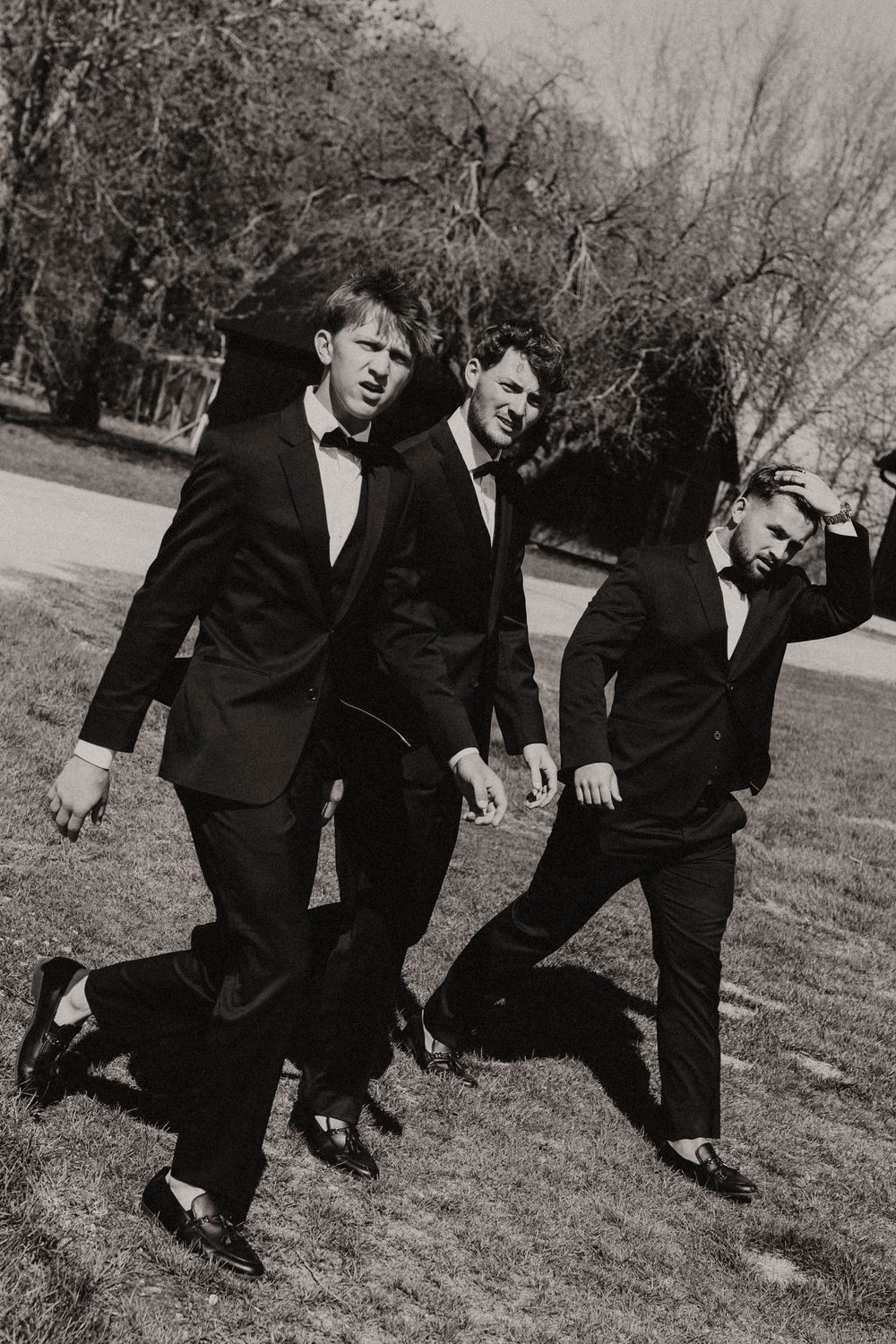 Black and white photo of groomsmen running and jumping on grass.