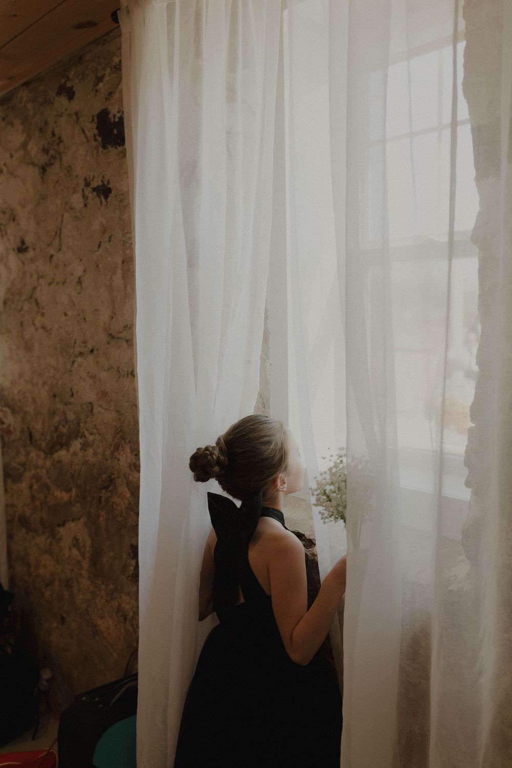 Silhouette of person peeking through sheer white curtains in rustic room.