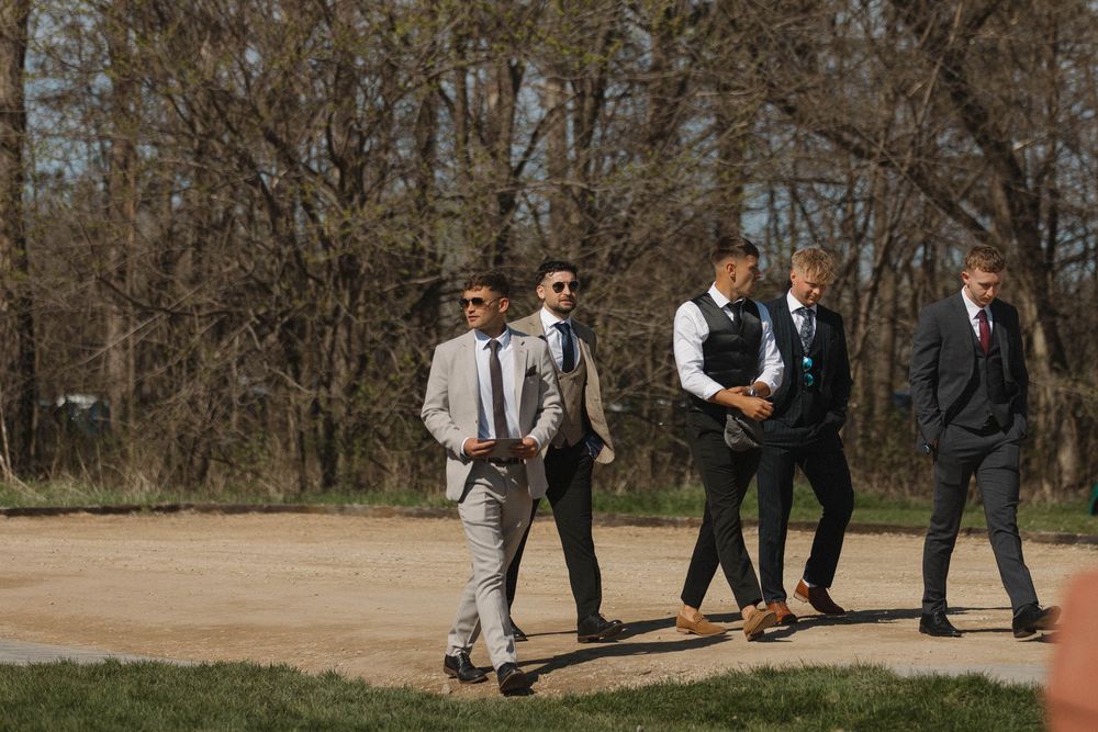 Wedding guests gather outside a rustic venue on a sunny day.