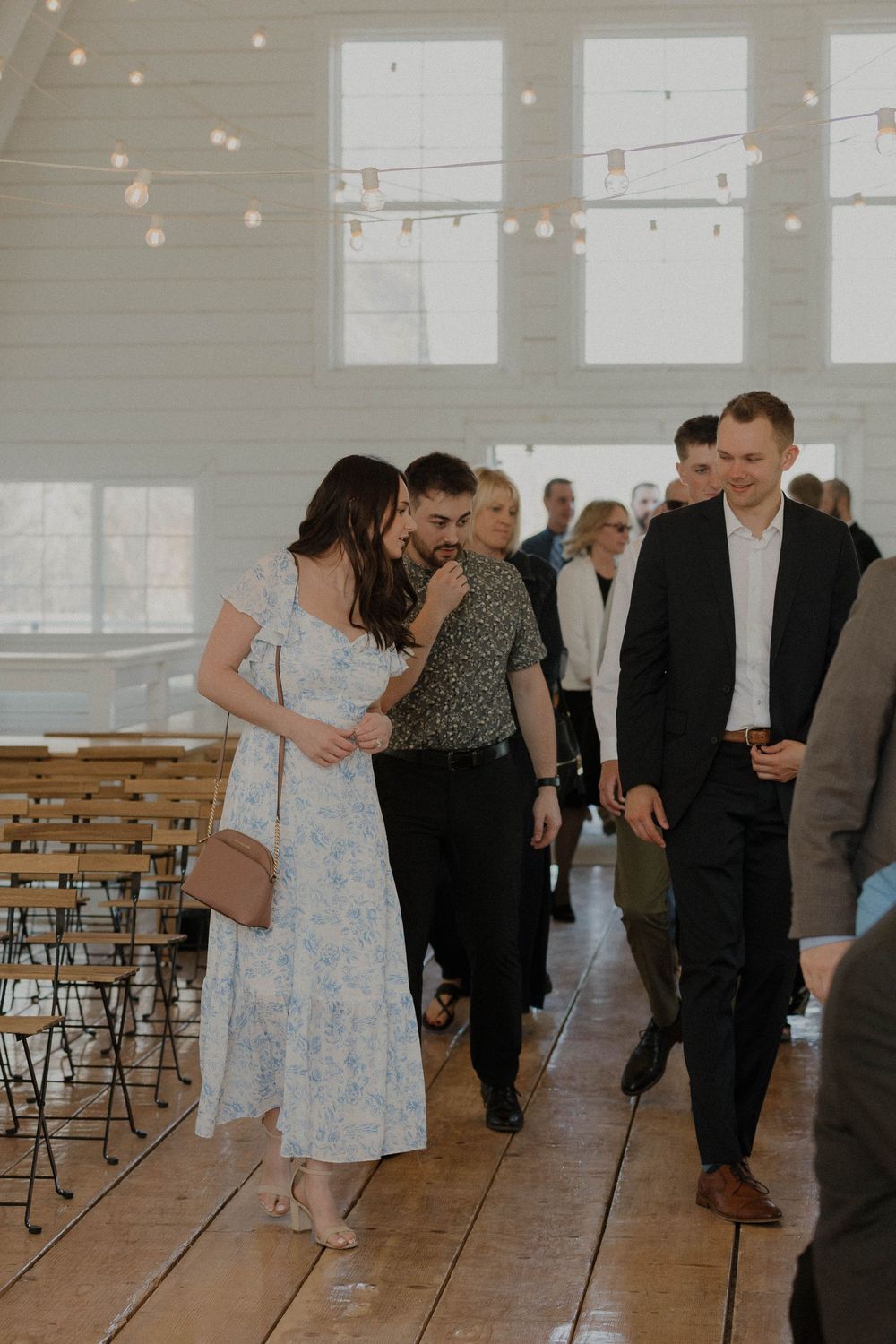 Wedding guests dance in a bright indoor venue with string lights and wooden floors.
