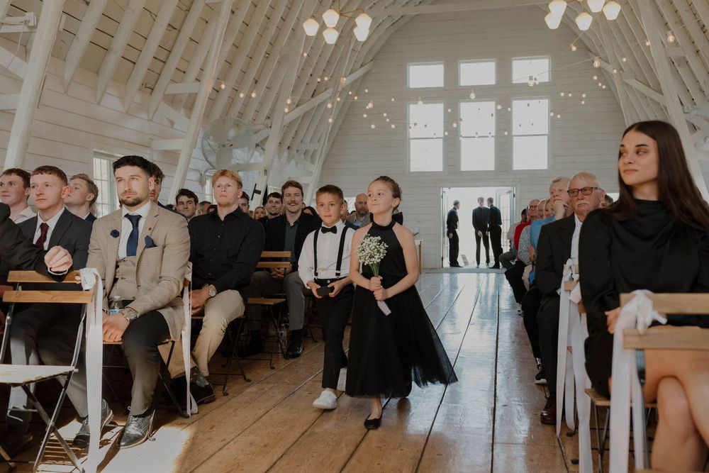 Interior of white chapel with string lights and guests during wedding ceremony.