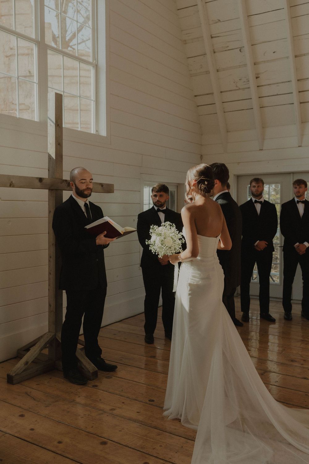 Wedding ceremony in progress inside a minimalist white chapel with hardwood floors.