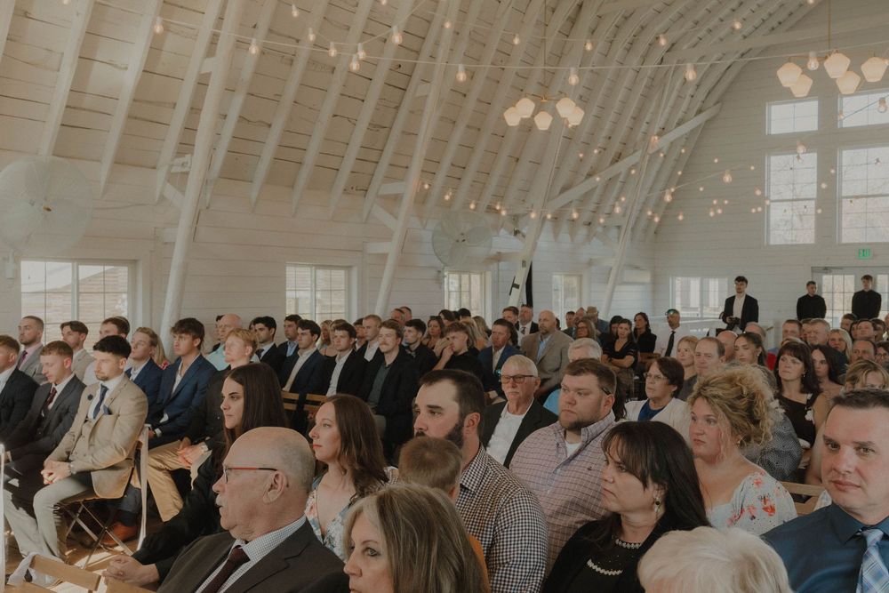 Wedding guests fill a bright, modern venue with vaulted ceilings and large windows.