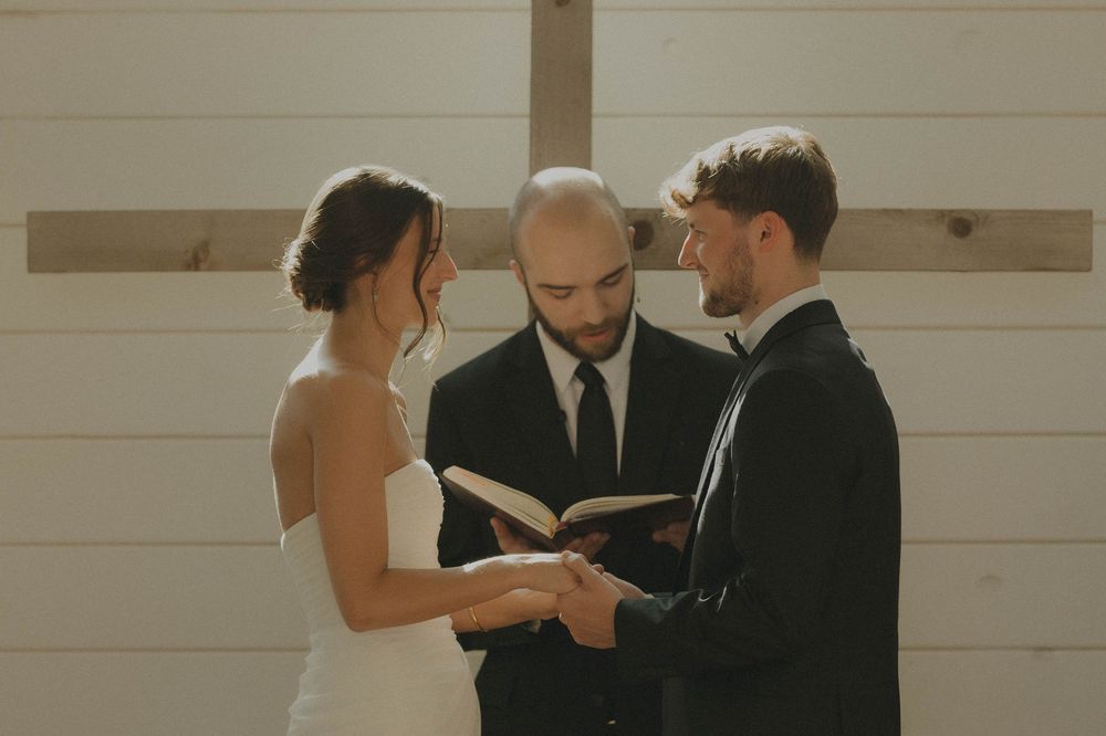 Wedding ceremony participants gather in an intimate moment inside a white-walled venue.