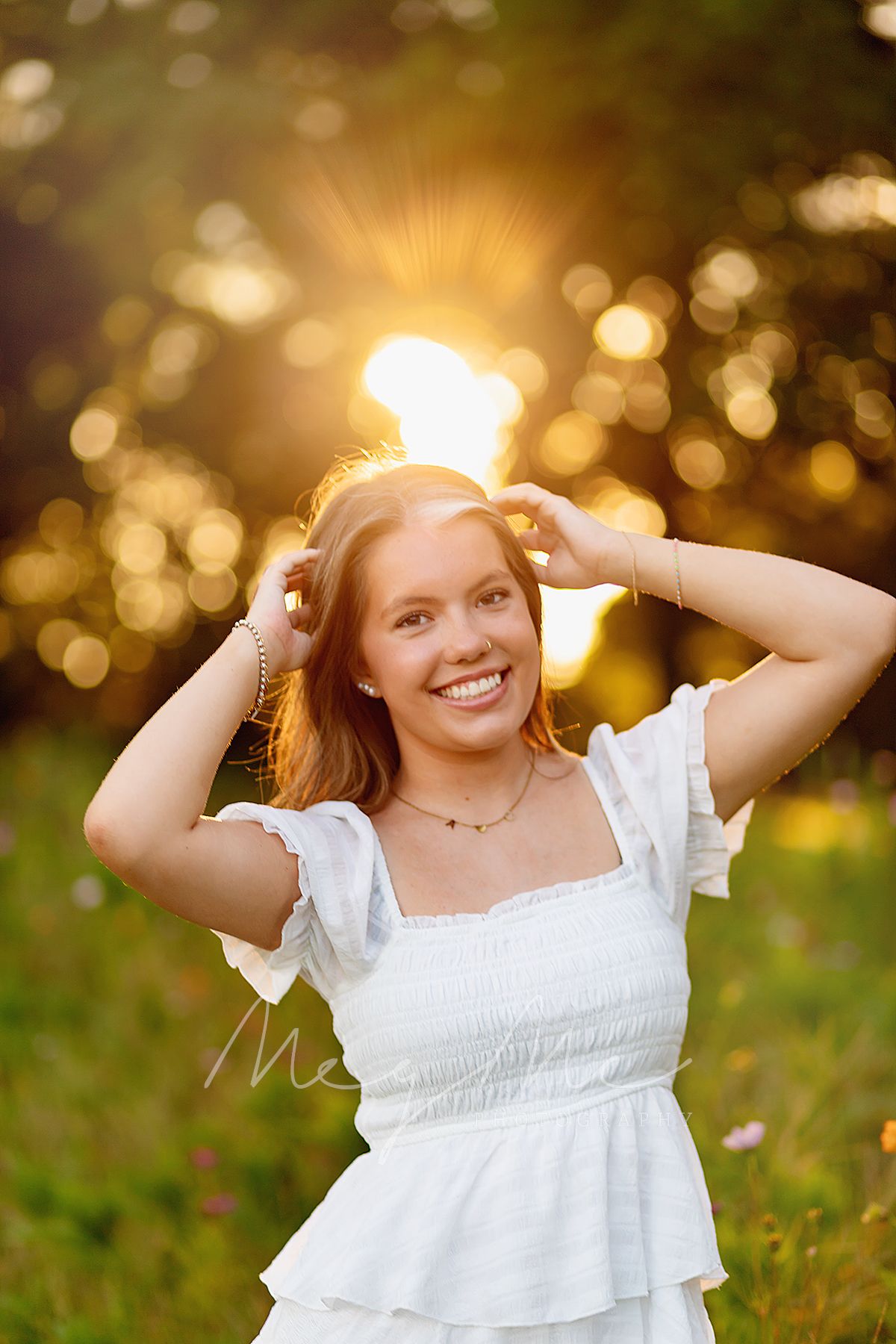 A teen in a white dress sits in golden sunlit flower field during sunset. Senior pictures in Medina, TN with MegMc Photography
