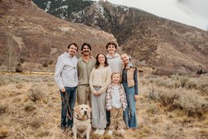 Family and golden retriever posing together in front of rugged mountain landscape on sunny autumn day.