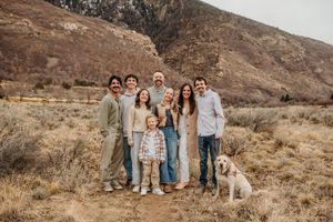 A group poses together with their dog against a brown mountain landscape in casual earth-toned clothing.