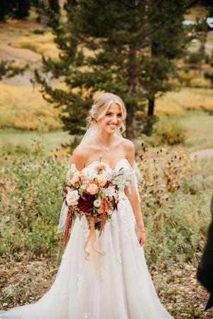 Bride in strapless white gown smiles while holding vibrant autumn bouquet with burgundy and peach flowers.