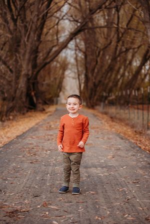A series of four outdoor photos showing a child in an orange sweater and brown pants walking down a leaf-covered path.