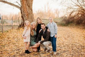 A family sits together surrounded by fallen autumn leaves during a seasonal outdoor photo session at sunset.