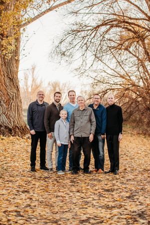 Group portrait captured outdoors in autumn with fallen orange leaves scattered on the ground and trees in the background.