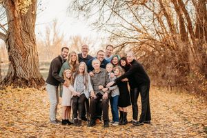 Extended family poses together for outdoor autumn portraits in a golden-hued wooded area during fall season.