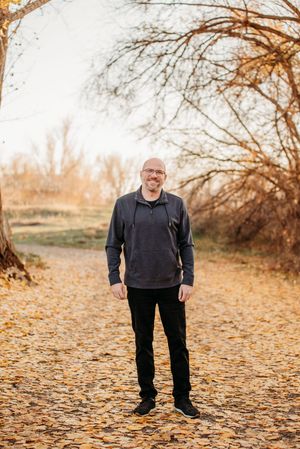 Person standing on fallen autumn leaves along a dirt path surrounded by bare trees in warm golden lighting.