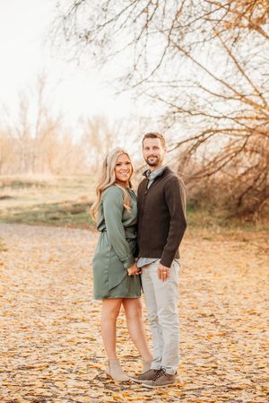 A couple shares a tender moment among autumn leaves in a natural outdoor setting during golden hour.