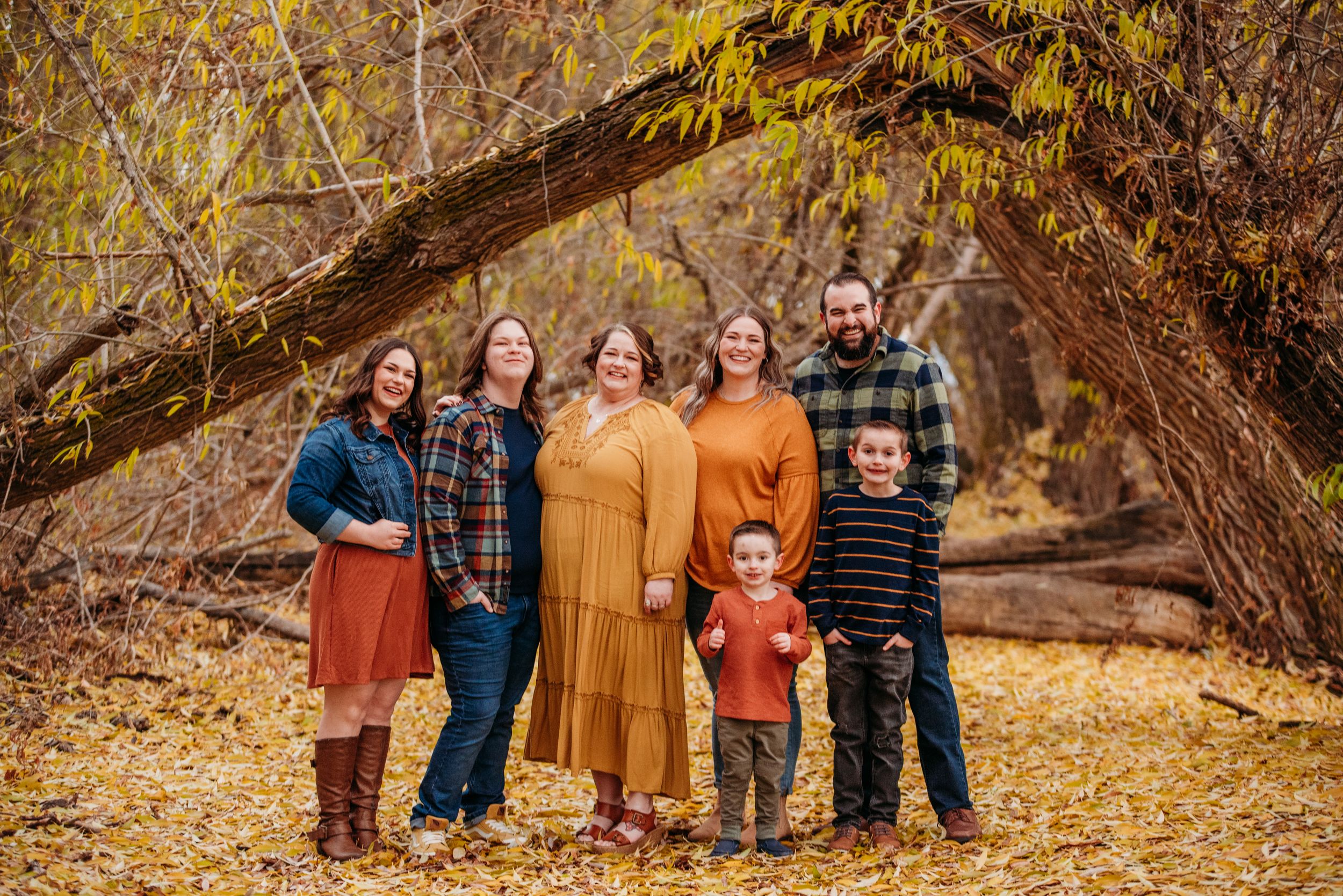Group portrait in fall setting with yellow leaves and natural archway of branches overhead.