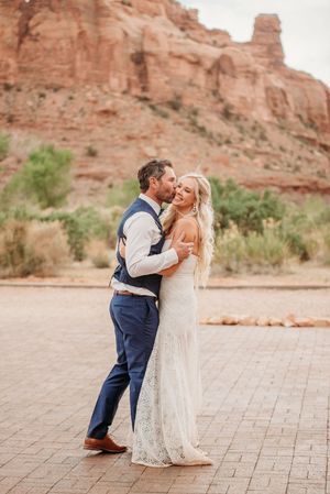 A romantic couple shares an intimate moment on a brick patio with dramatic red rock cliffs in the background.