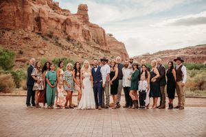 A large group gathered for a formal occasion against stunning red rock cliffs in a desert landscape.
