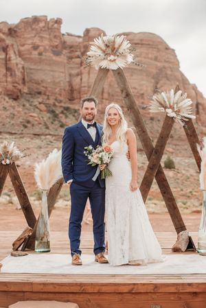 A wedding ceremony setup features dried palm flowers and wooden arch backdrop against majestic red rock formations.