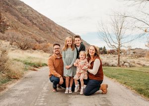 Family photo session on a dirt path with mountains and desert landscape in the background during golden hour.