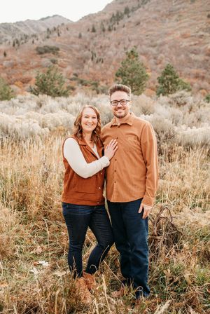 Couple shares romantic moments together in outdoor autumn setting with brown mountains and tall grass.