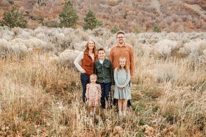 Family poses together in casual fall outfits among dried grass and brush on a hillside.