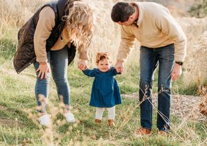 Family candid moments captured outdoors in a natural setting with sunlit grass and trees.