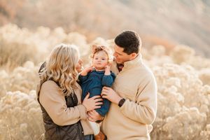 A family of three embraces while sharing a tender moment in golden sunlight.