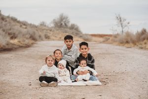 A group sits together on a blanket on a desert dirt road surrounded by brush on an overcast day.