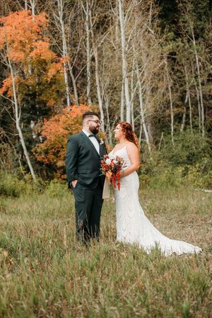 Wedding couple poses in front of vibrant orange fall foliage and white birch trees.