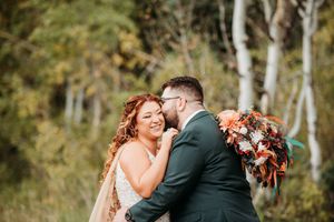 A joyful couple embraces outdoors in an autumn forest setting with fall-colored floral bouquet.