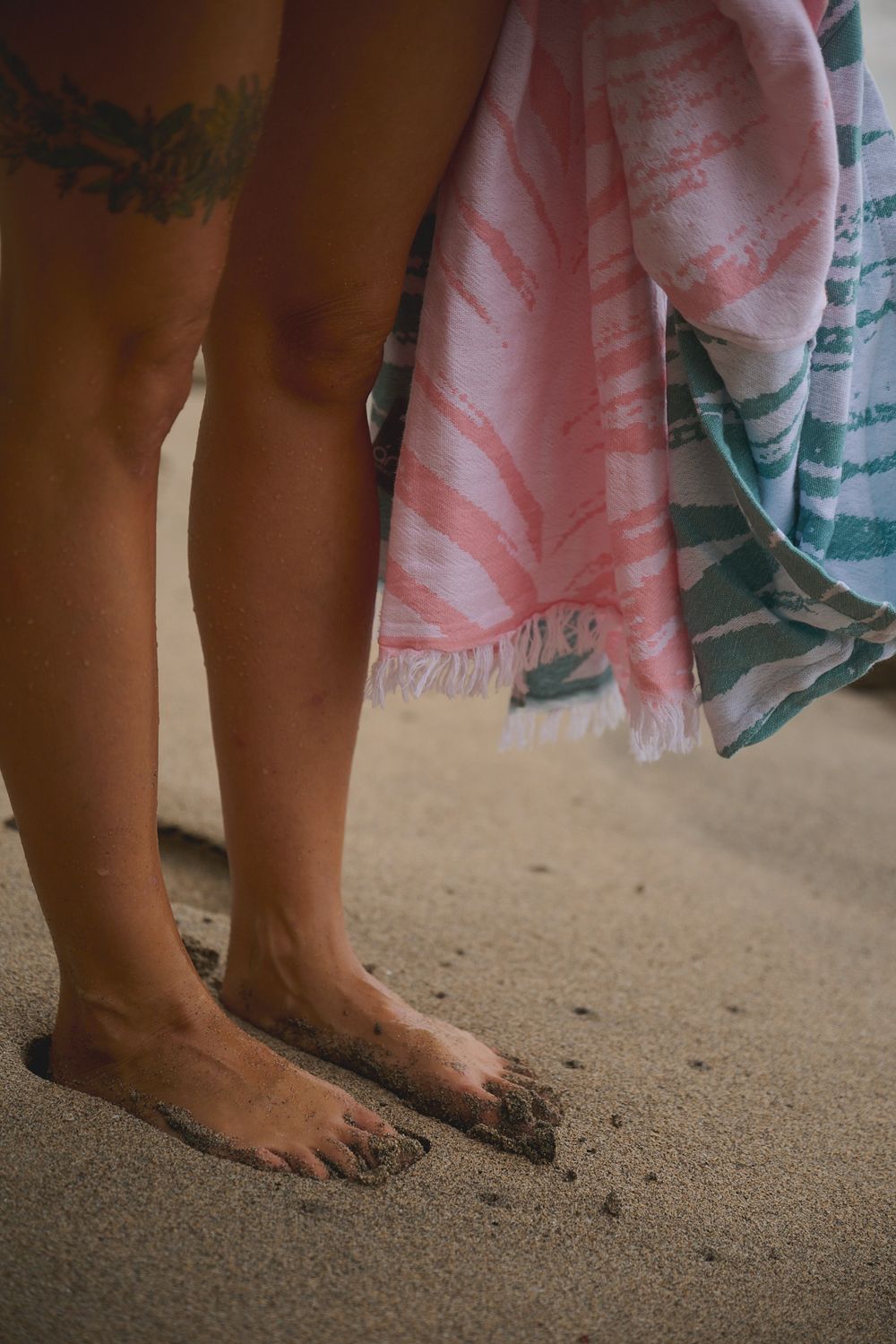 Bare feet standing in sand with colorful beach towels draped in the background.