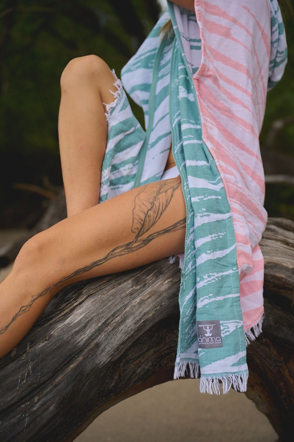 A person's arm with a floral branch tattoo rests on a surface next to a pink and turquoise striped beach towel.