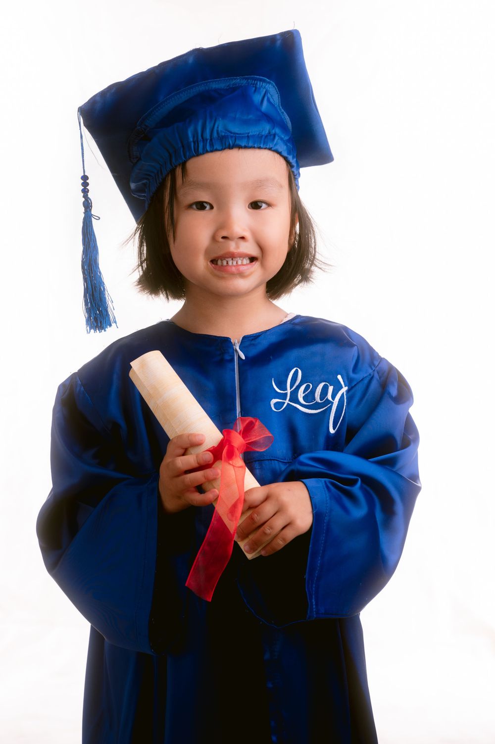Young graduate in royal blue cap and gown holding diploma while smiling in multiple poses.