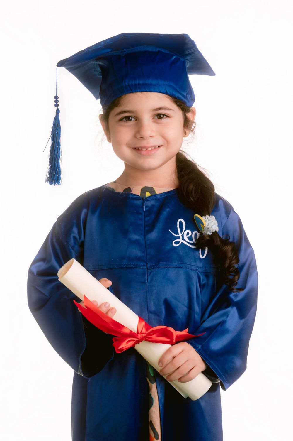 Young graduate in blue cap and gown holding diploma with red ribbon against white background.