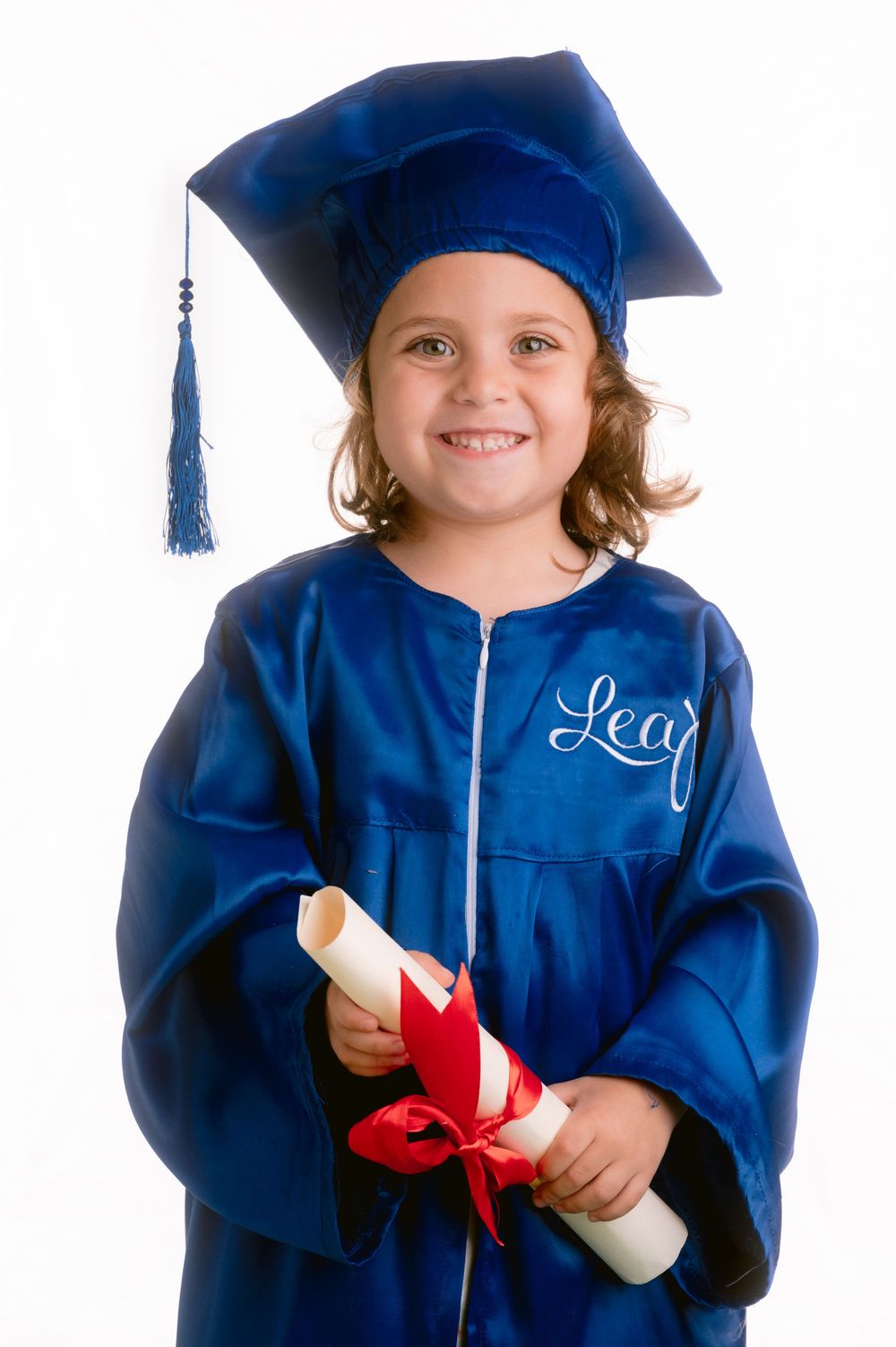A graduate in blue cap and gown holding a diploma with red ribbon against white background.
