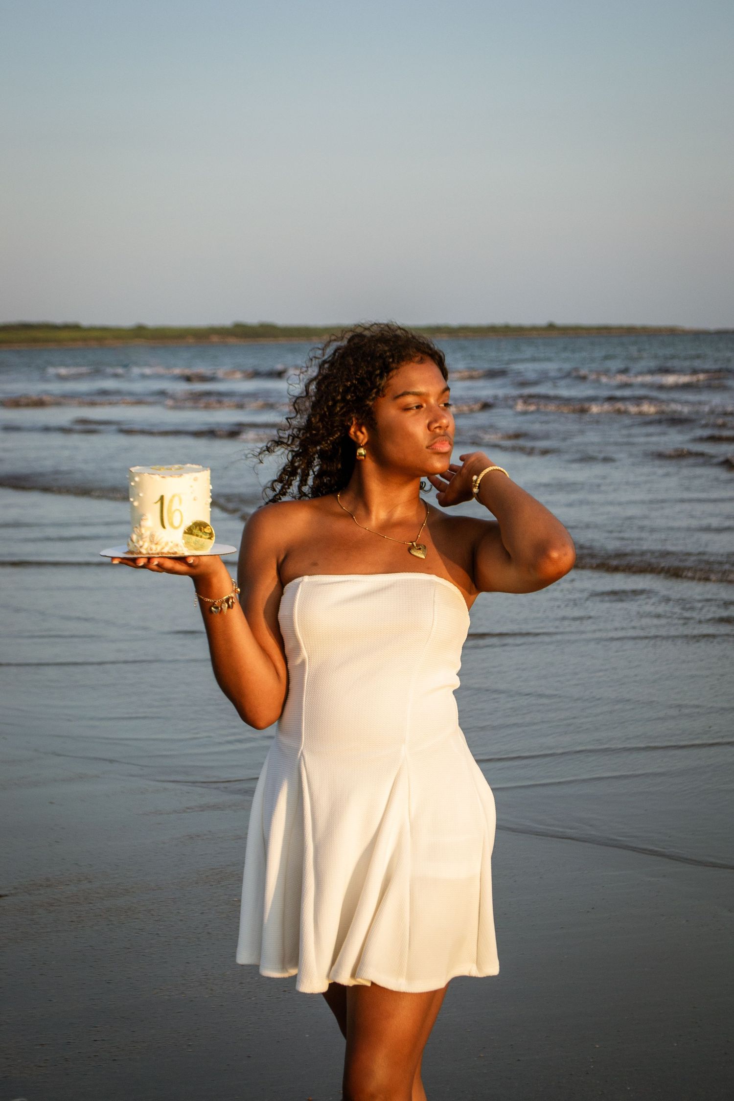 Person holds glowing lantern on beach during golden hour sunset.